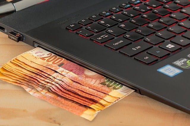 Geld wird in einen Laptop eingeführt.