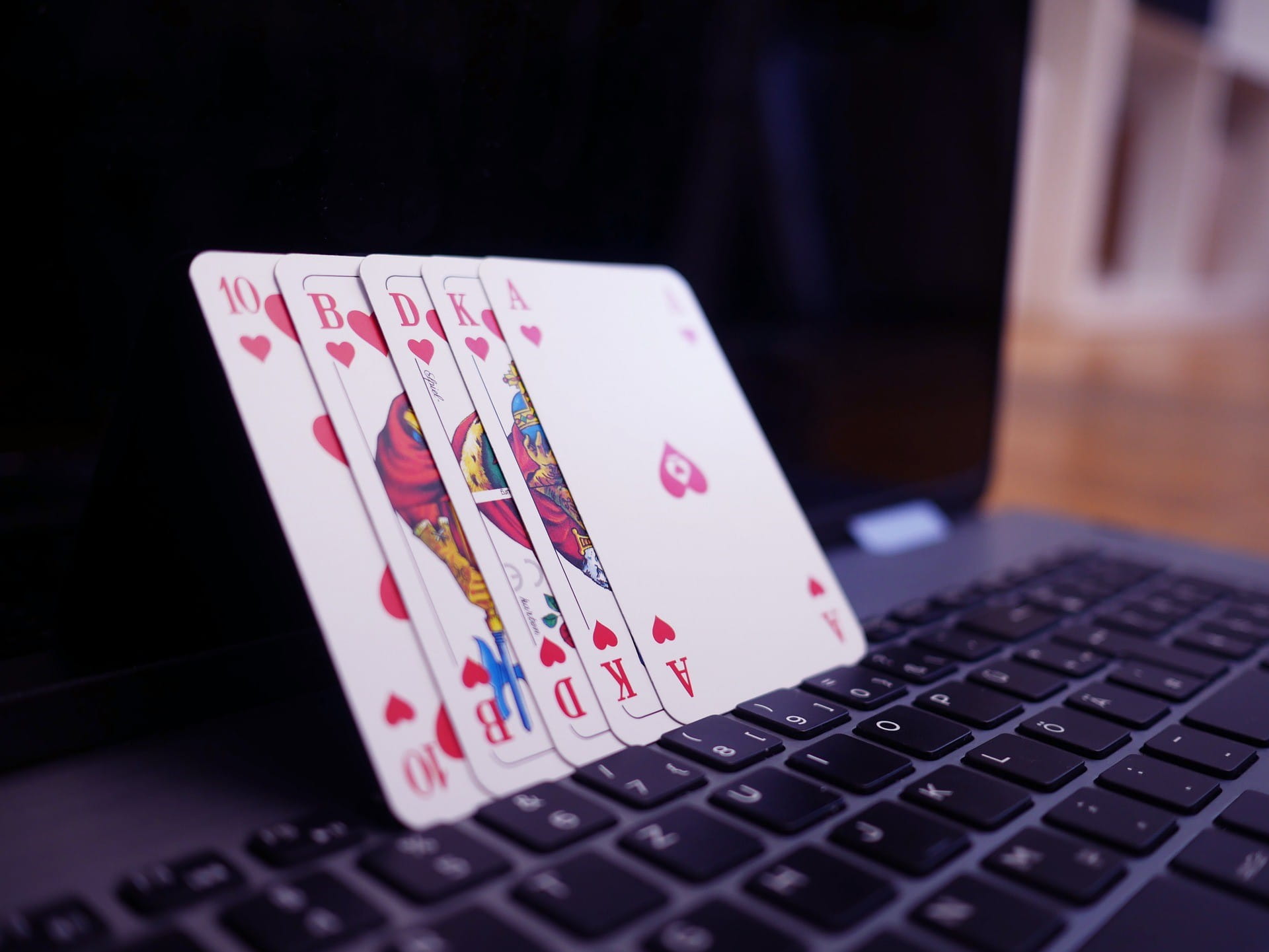Fünf Pokerkarten stehen auf einem offenen Laptop.