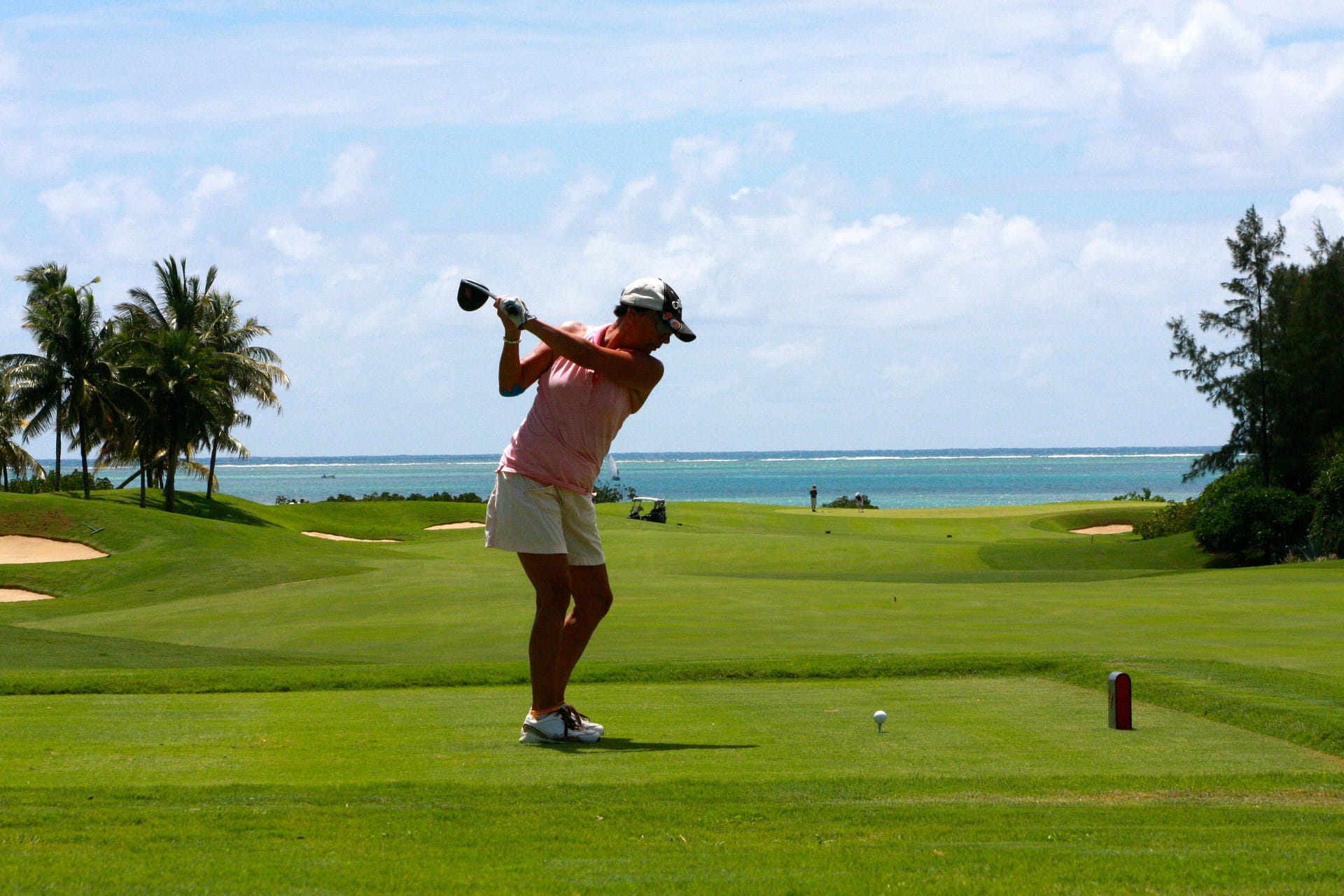 Eine Golfspielerin schwingt den Schläger auf dem Golfplatz. Im Hintergrund ist Wasser zu sehen.