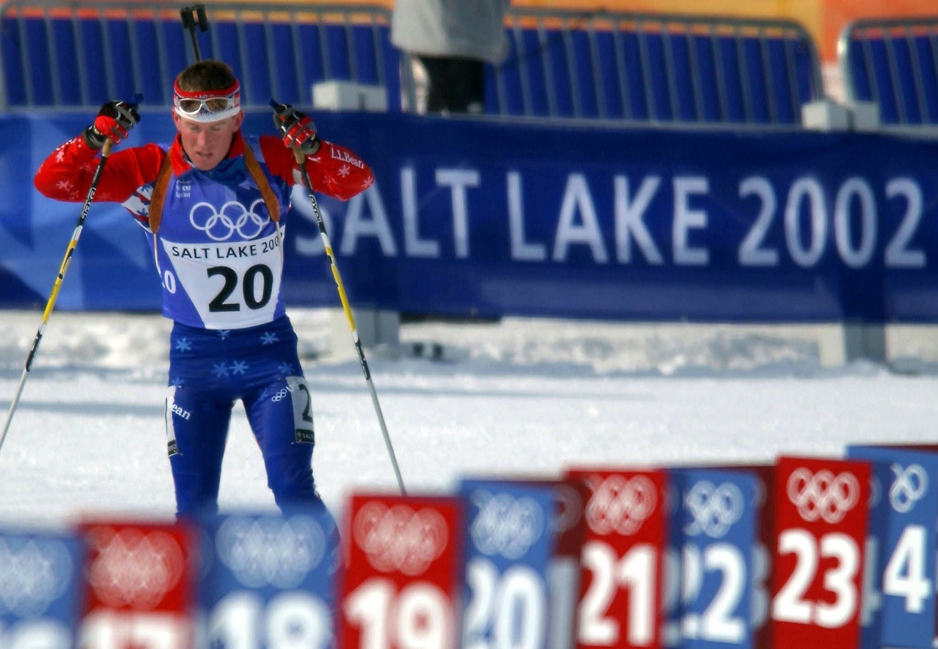 Ein Biathlon-Athlet beim Langlaufen vor einem Plakat mit der Aufschrift Salt Lake 2002.