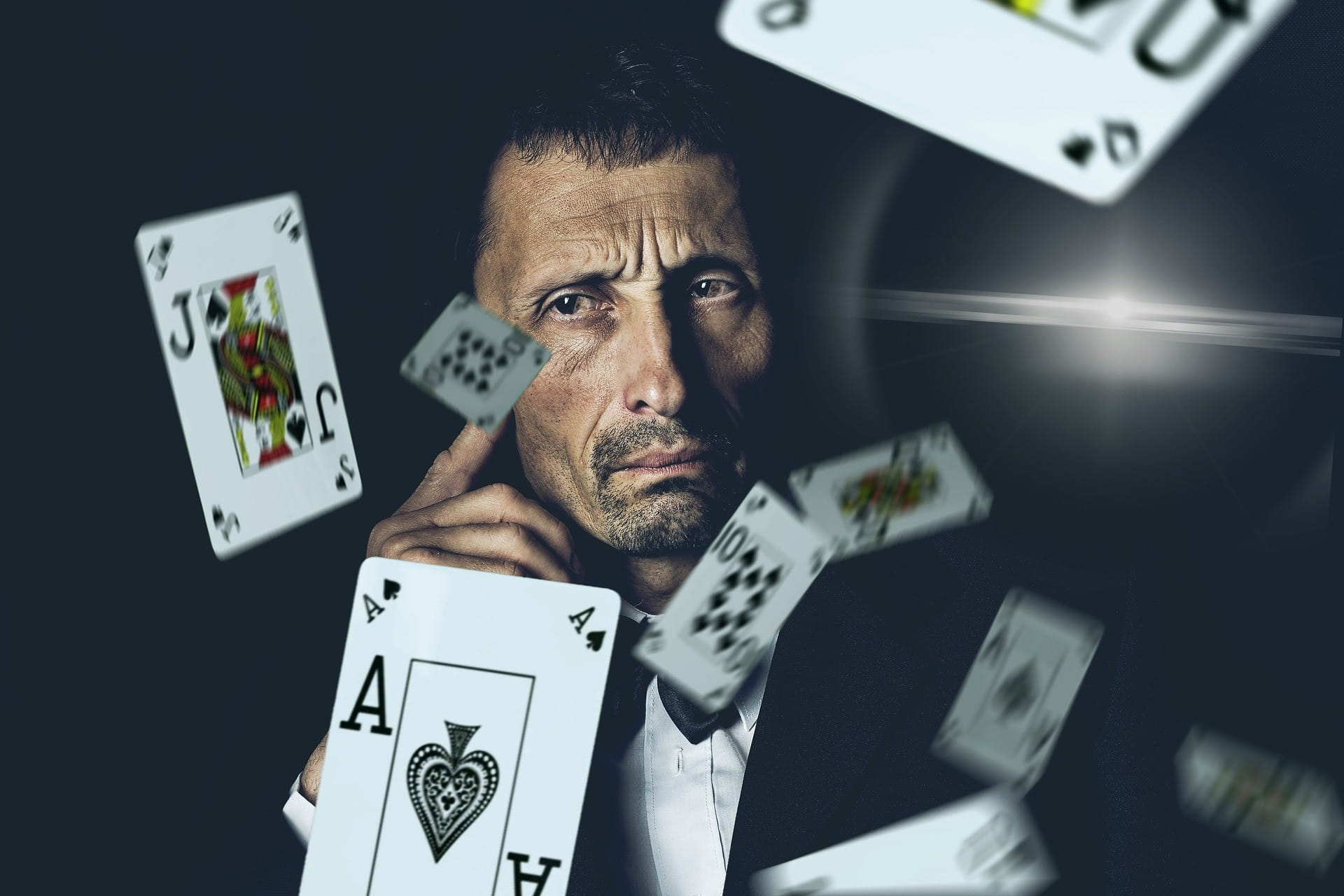 Vor einem ernst schauenden Mann fliegen mehrere Pokerkarten durch die Luft.