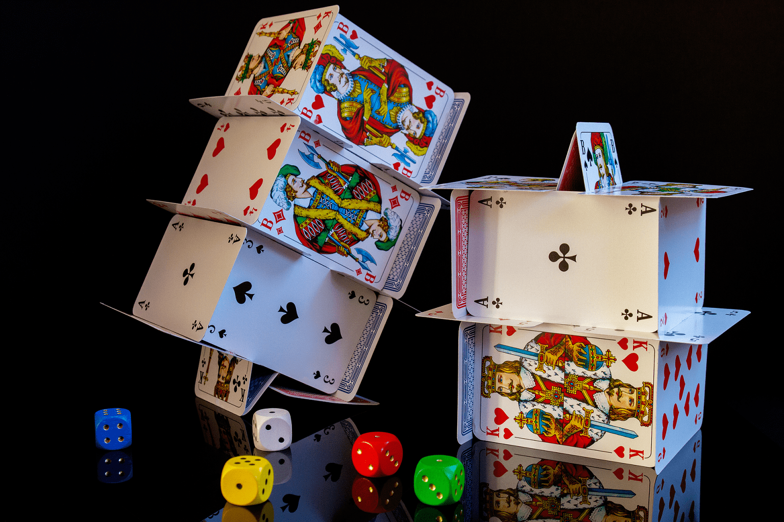Aus mehreren Pokerkarten wurden zwei mehrstöckige Kartenhäuser gebaut. Davor liegen fünf Würfel mit unterschiedlichen Farben.