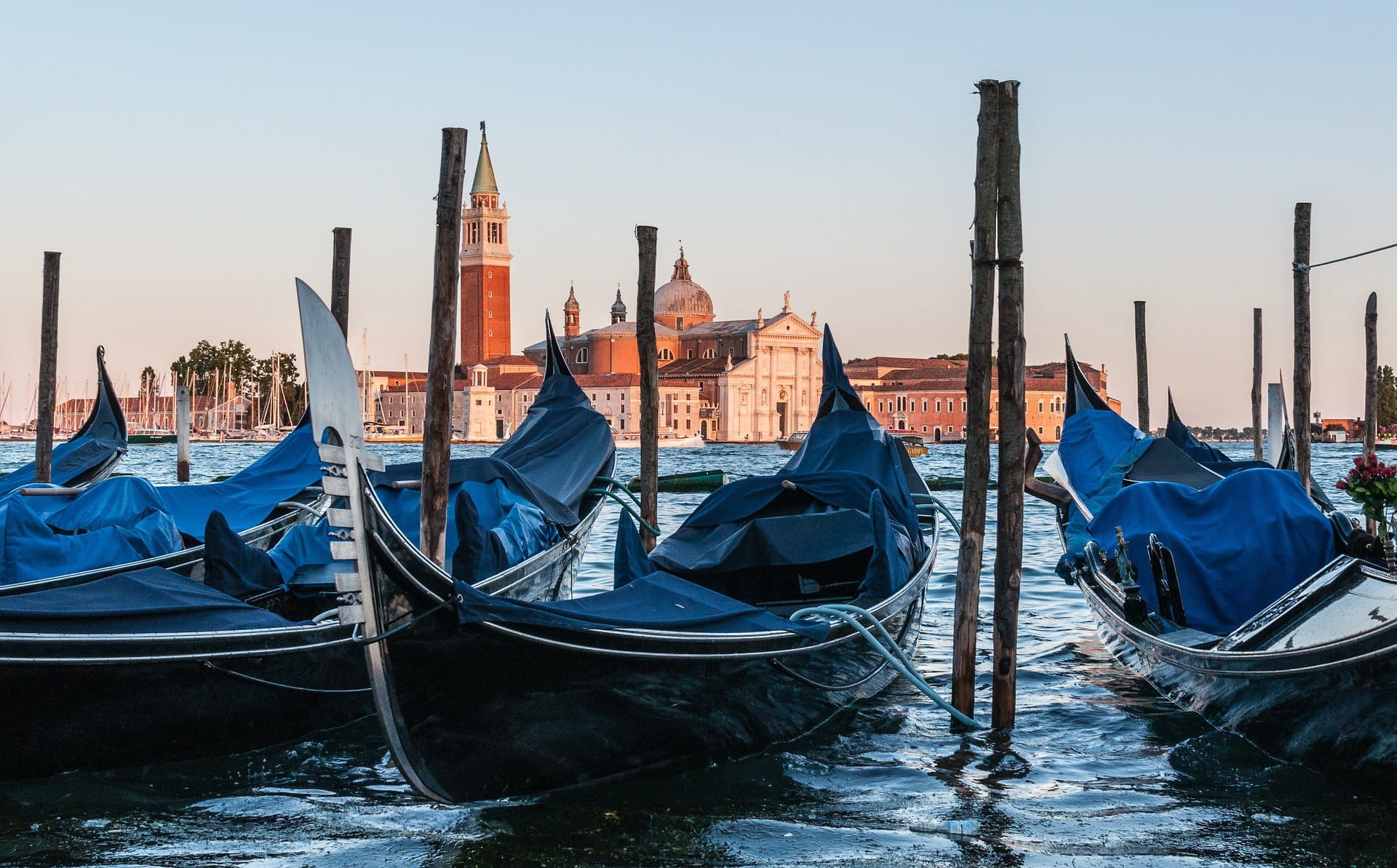 Im Hintergrund ist Venedig zu sehen – im Vordergrund stehen drei Gondeln auf dem Wasser.