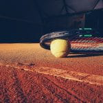 Ein Tennisschläger liegt in einer Tennishalle auf dem Boden, unter ihm liegt der Ball.