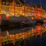 Eine dänische Stadt bei Nacht: vor den beleuchteten Häusern liegen kleine und mittelgroße Boote.