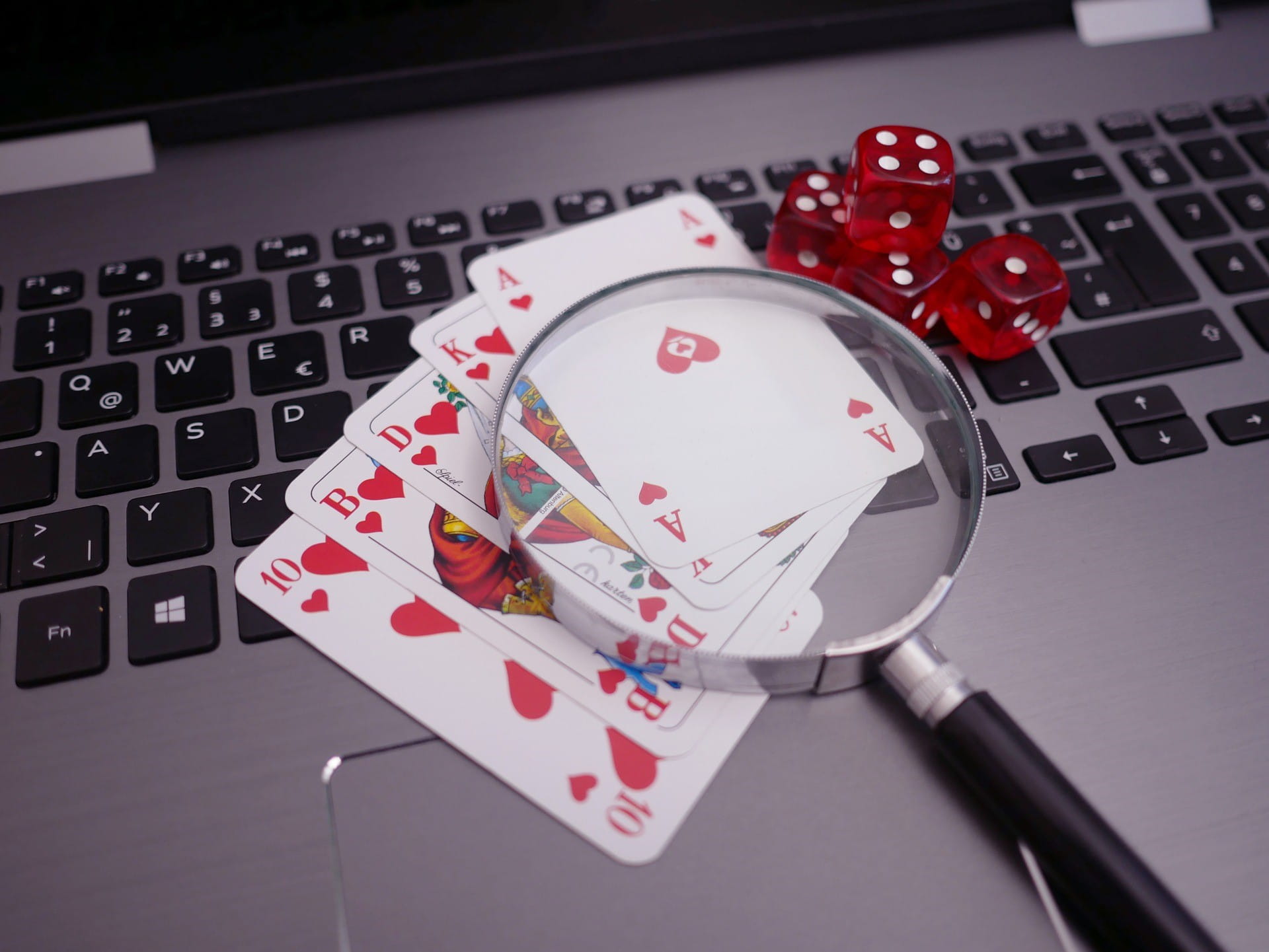 Auf einer Tastatur liegen Pokerkarten, vier rote Würfel und eine Lupe.