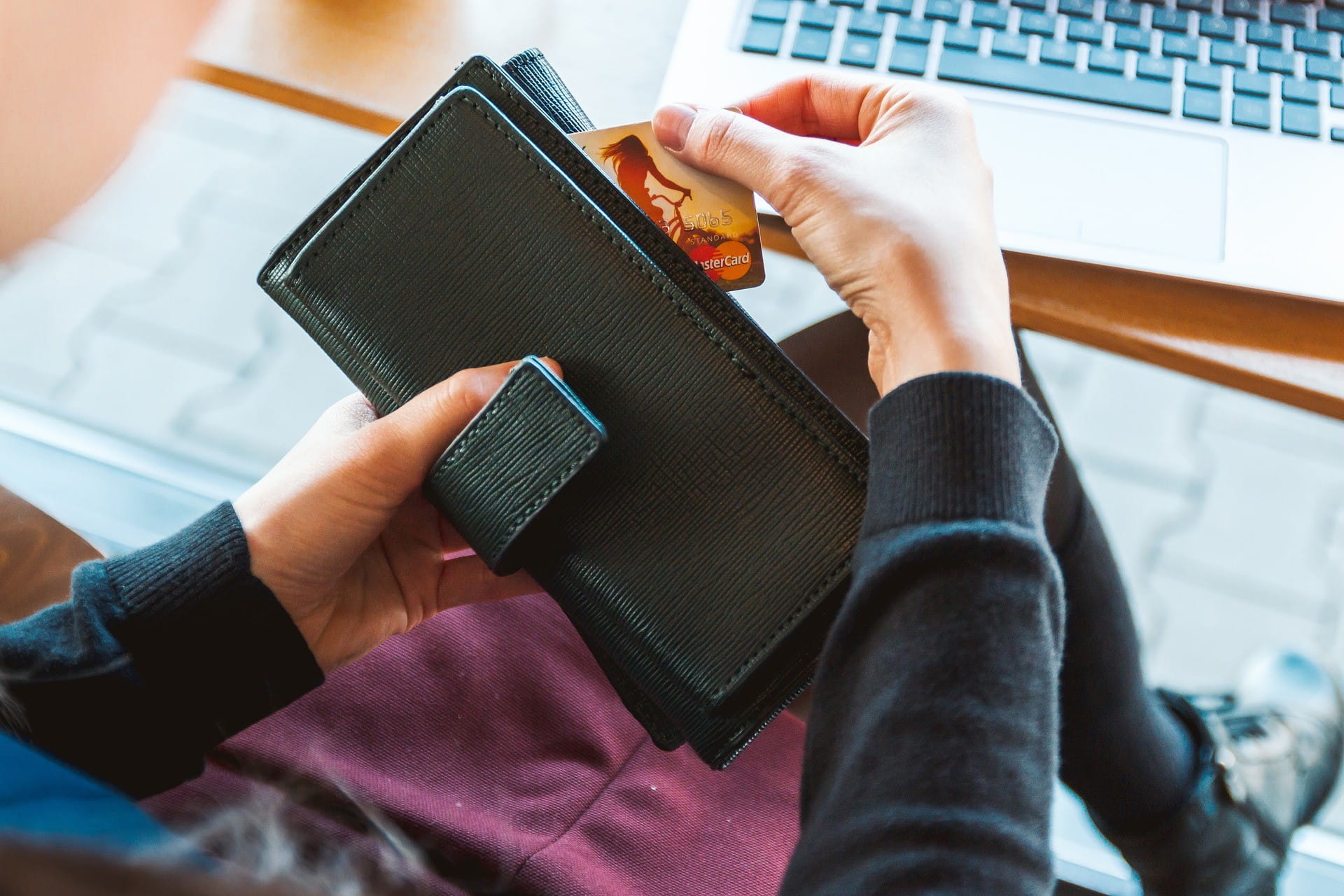 Eine Person hält mit der linken Hand den Geldbeutel und holt mit der rechten Hand eine Kreditkarte raus.