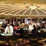 In einem Casino stehen mehrere Roulette-Tische, die von vielen Spielern besucht sind.