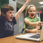 Ein Junge und ein Mädchen sitzen vor einem Laptop und freuen sich.