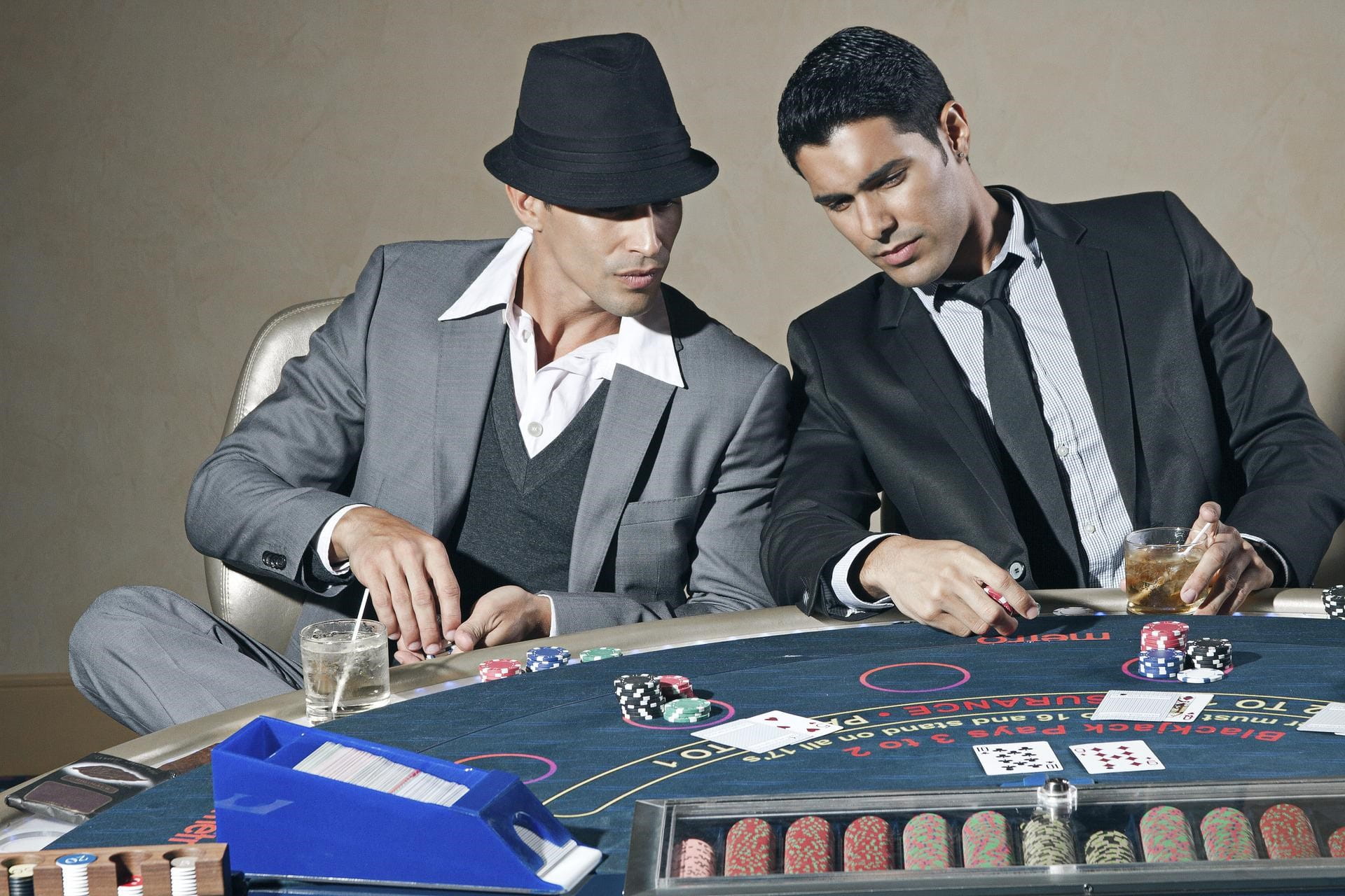 Zwei elegant gekleidete Männer sitzen an einem Pokertisch und besprechen sich.