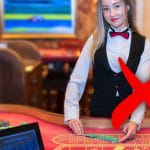 Eine Live Casino Dealerin an einem Spieltisch, davor ein rotes Kreuz.