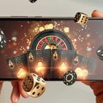 Ein Smartphone in zwei Händen gehalten, darauf ist ein Roulette-Kessel sowie Spielchips und Karten zu sehen.