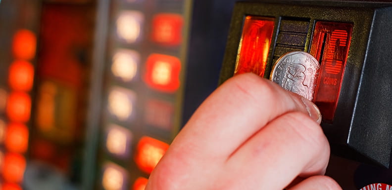 Eine Hand, die eine Münze in einen landbasierten Spielautomaten steckt.