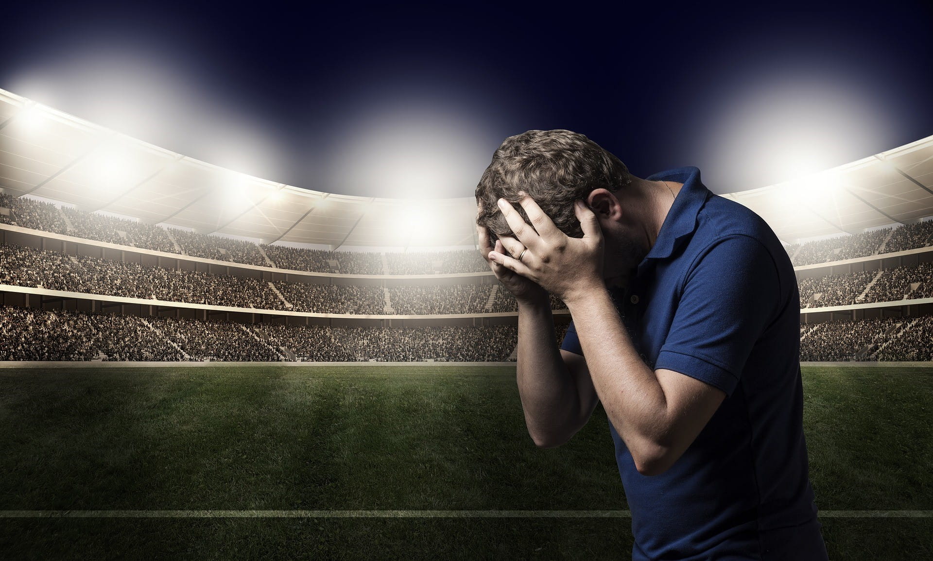 Ein Mann steht mit gesenktem Kopf und seinen Händen vor dem Gesicht in einem Fußballstadion.