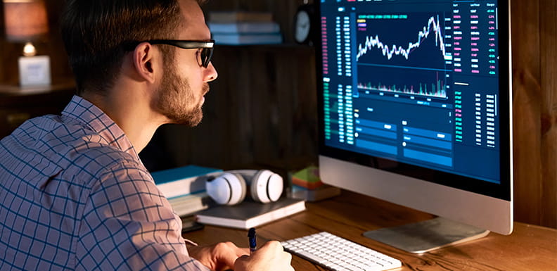 Ein Mann sitzt vor einem Computerbildschirm, auf dem ein Aktienkurs zu sehen ist.