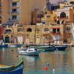 Kleine bunte Fischerboote schwimmen vor einer maltesischen Kleinstadt.