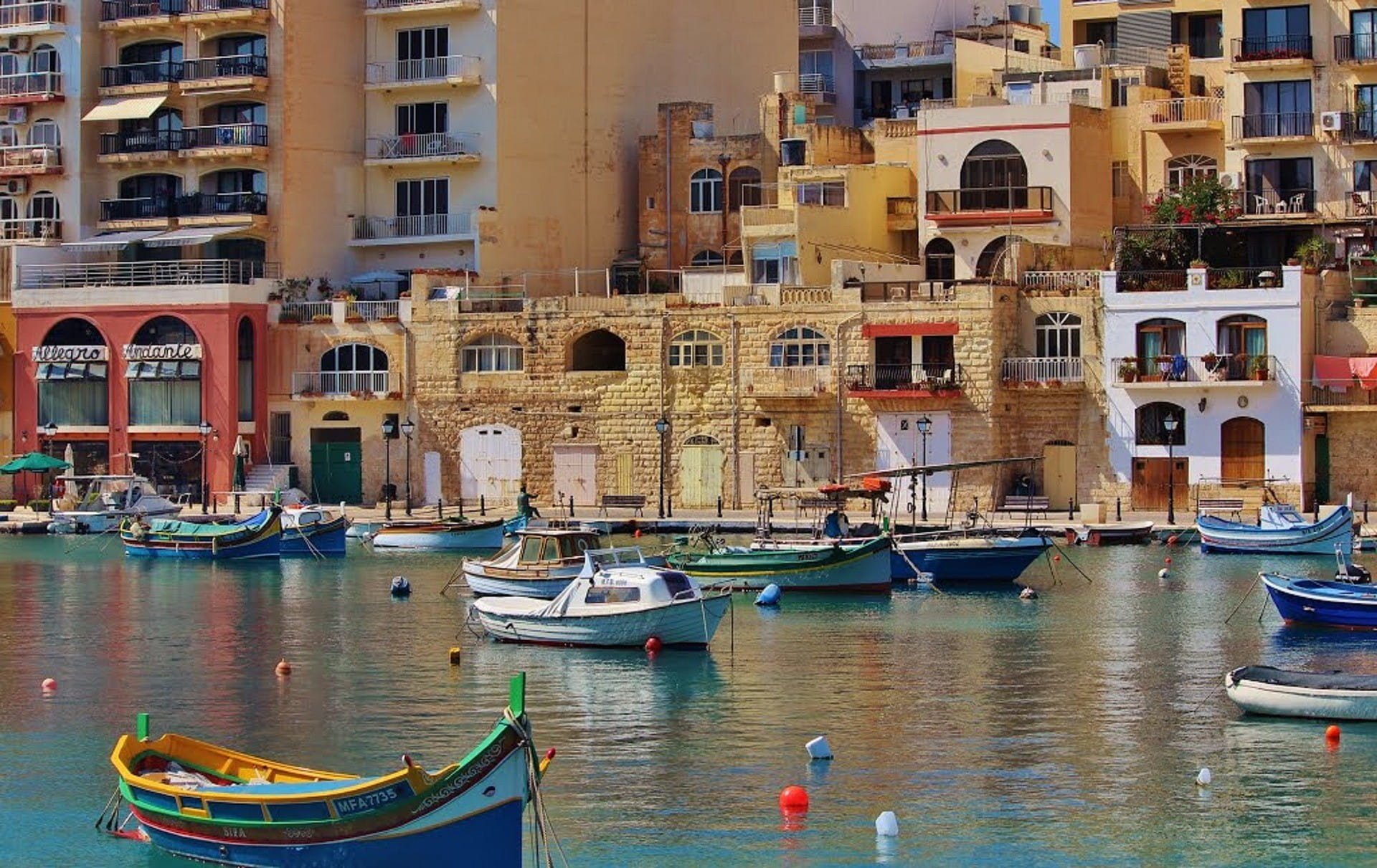 Perahu nelayan kecil berwarna-warni mengapung di depan kota kecil Malta.