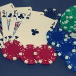 Fünf Pokerkarten und mehrere Spielchips unterschiedlicher Farben liegen auf einem Tisch.