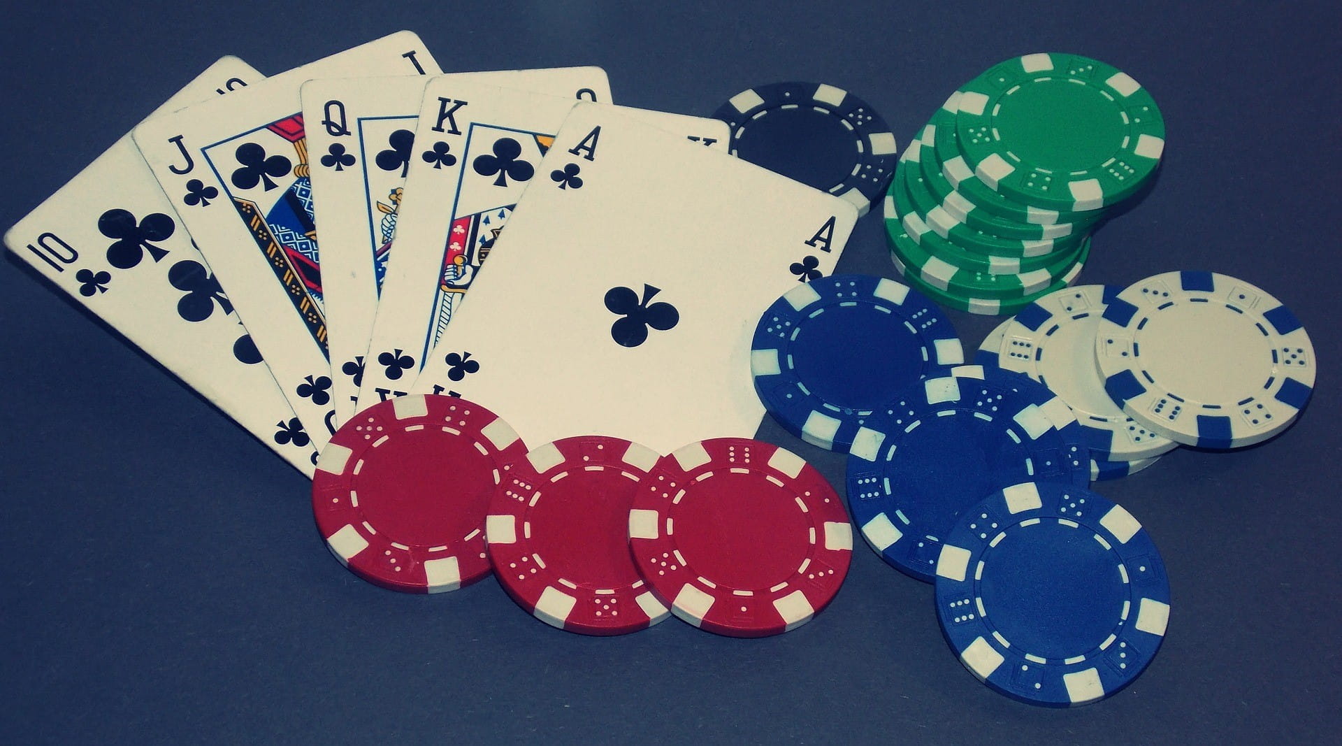 Lima kartu poker dan beberapa chip bermain dengan warna berbeda terletak di atas meja.