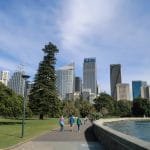 Spaziergänger im Park von Sydney vor einigen Hochhäusern.