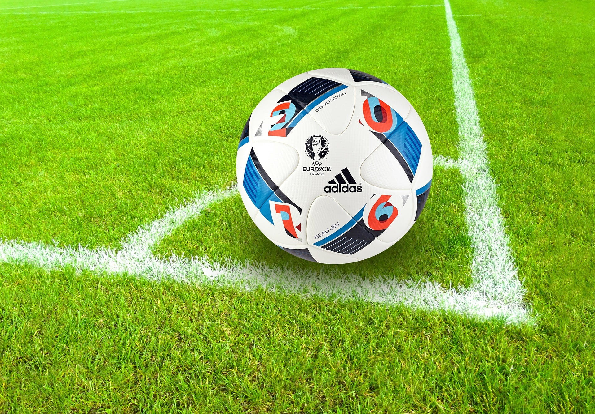 Di sudut lapangan sepak bola terdapat bola sepak yang di atasnya tercetak logo beberapa klub olahraga.