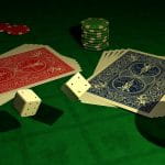 Auf einem Tisch mit grüner Fläche liegen zwei Stapel Pokerkarten, Spielchips und vier Würfel neben einem leeren Weinglas.
