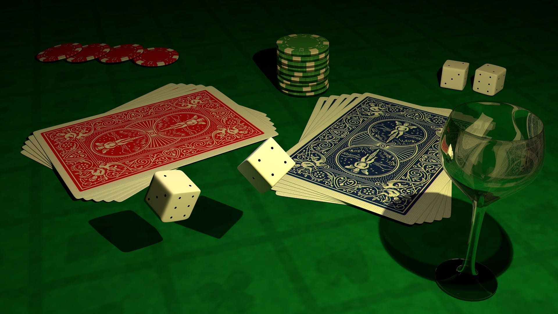 Dua tumpukan kartu poker, chip remi, dan empat dadu tergeletak di atas meja dengan permukaan hijau di samping gelas anggur kosong.