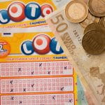 Auf zwei Lottoscheinen liegen viele Münzen und ein 50-Euro-Schein.