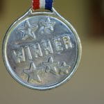 Auf einer silbernen Medaille sind fünf Sterne und das Wort Winner vorhanden.