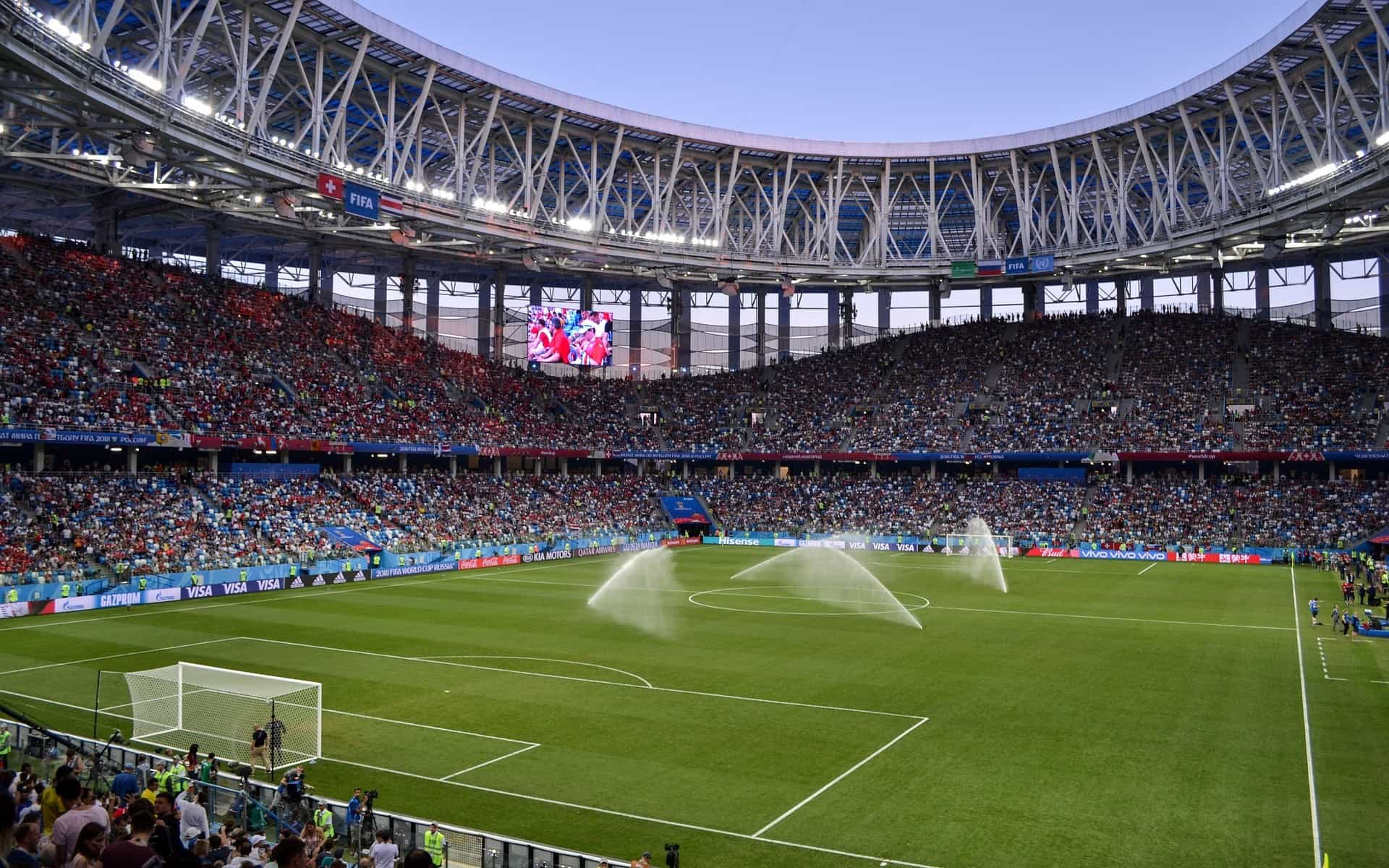 Das Feld eines voll besetzten Fußballstadions wird gerade bewässert.