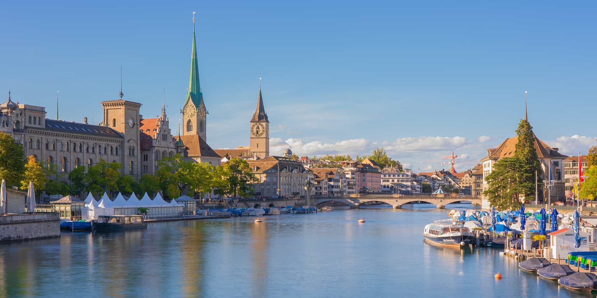 In Zürich stehen links und rechts eines Flusses Gebäude, während am Ufer Schiffe liegen.