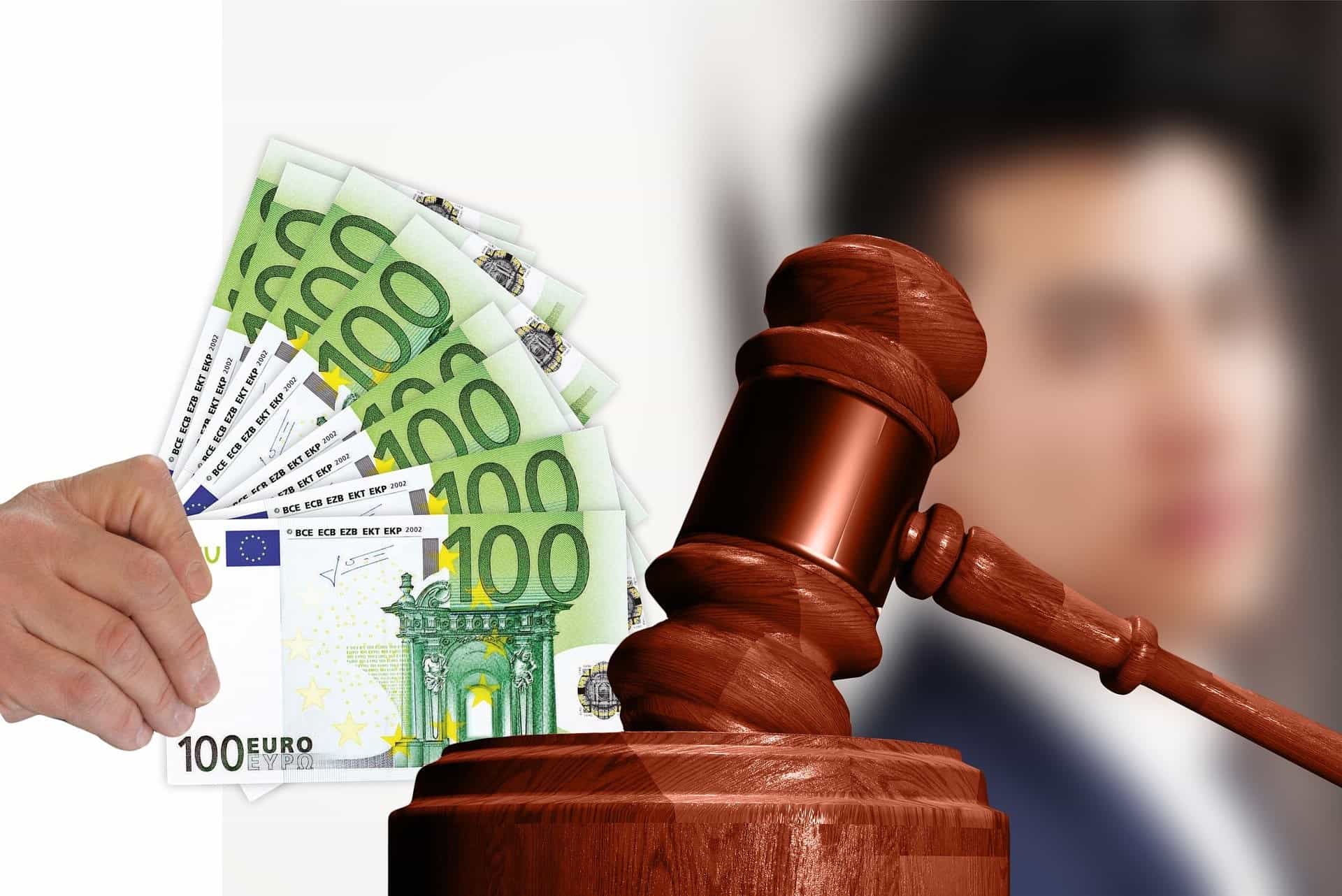 Links von einem Gerichtshammer hält eine Hand mehrere Einhundert-Euro-Scheine wie einen Fächer.