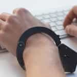 Die Hände einer männlichen Personen tragen Handschellen und liegen auf einer Tastatur.