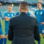Ein Mann im Anzug steht vor einer Gruppe Fußballern.