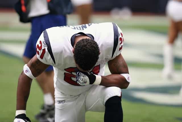 Seorang pemain NFL berdiri dengan satu lutut dan menundukkan kepalanya ke depan.