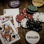 Auf einem Holztisch liegen drei Spielkarten, mehrere Spielchips und ein Chip mit der Aufschrift Dealer.