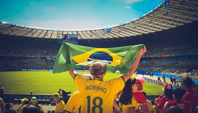 In einem Fußballstadion befinden sich Fußballfans, die eine brasilianische Fahne hochheben.