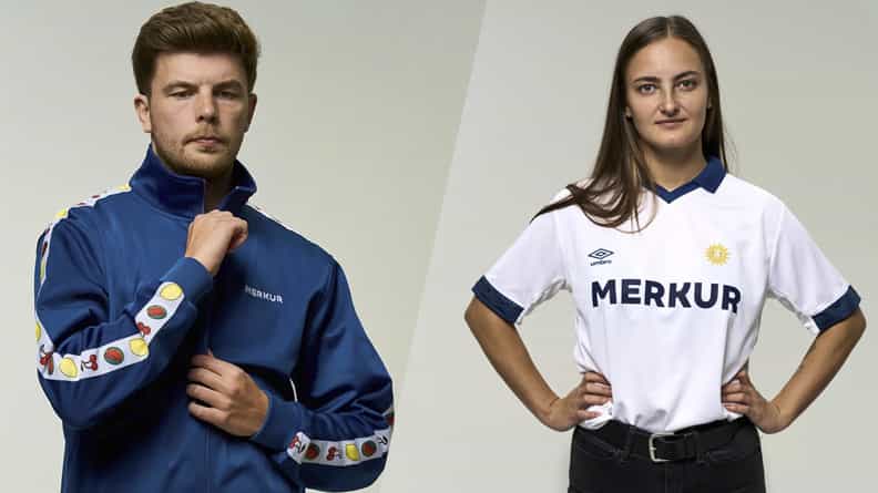 Der Merkur Streetwear Trainingsanzug ist petrol mit einem weißen Galonstreifen. Auf dem Galonstreifen finden sich Symbole aus dem Merkur Slot Fruitinator.