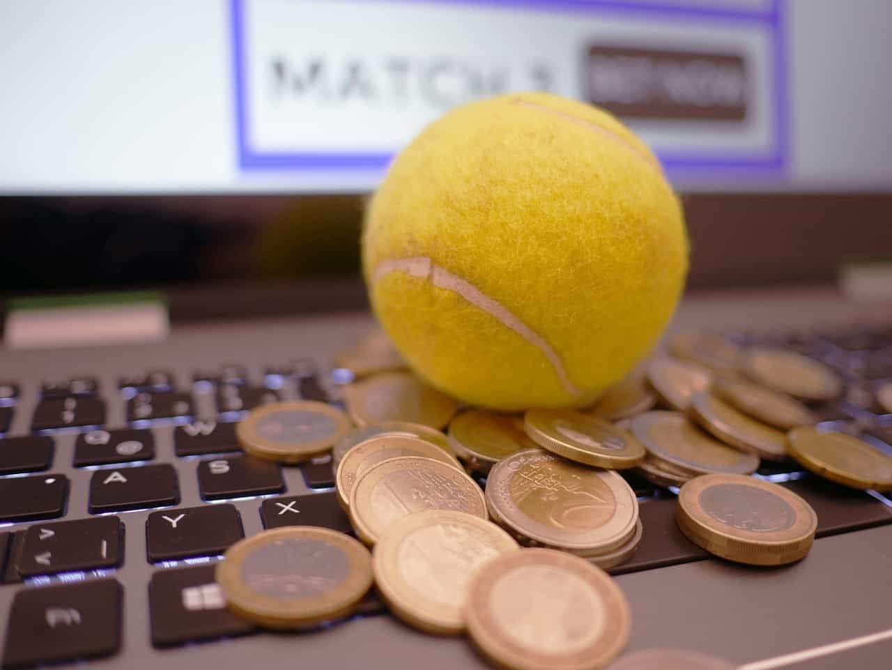 Tennisball und Euro-Münzen liegen auf einem Laptop.