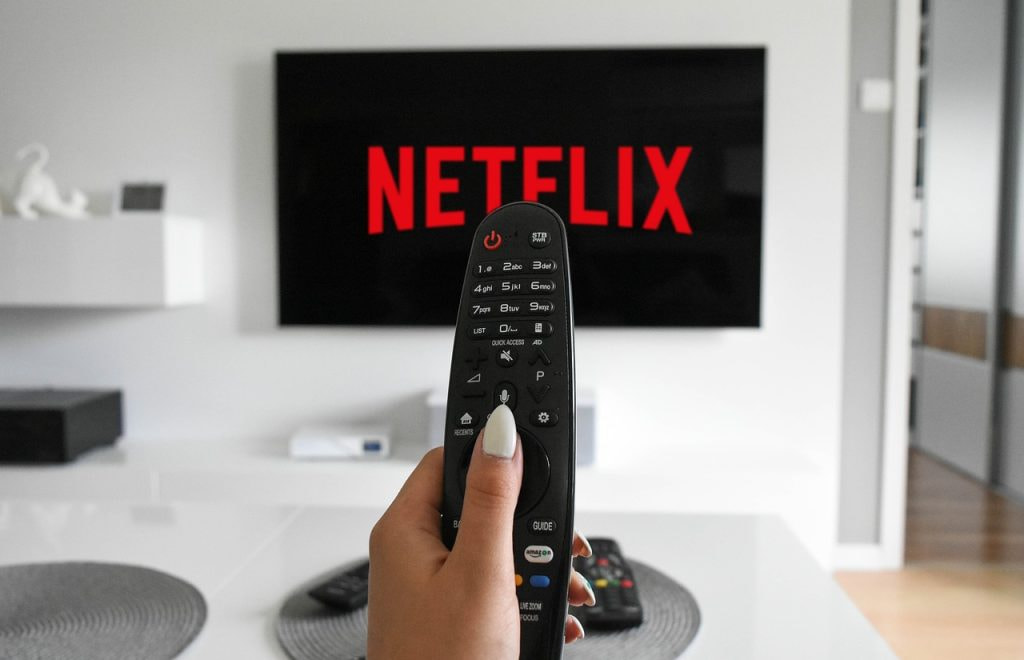 TV-Bildschirm, auf dem ein Netflix Logo zu sehen ist und eine Hand, die eine Fernbedienung hält.