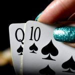 Eine Hand mit lackierten Fingernägeln, die zwei Spielkarten hochhält.