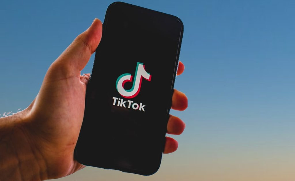 Mensch mit Smartphone in der Hand, auf dem ein Logo von TikTok zu sehen ist.