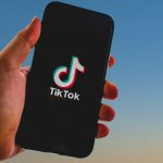 Mensch mit Smartphone in der Hand, auf dem ein Logo von TikTok zu sehen ist.
